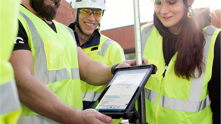 During a career at Infrakit, a team in neon yellow high-visibility vests review project updates on a tablet with plan and status details visible.
